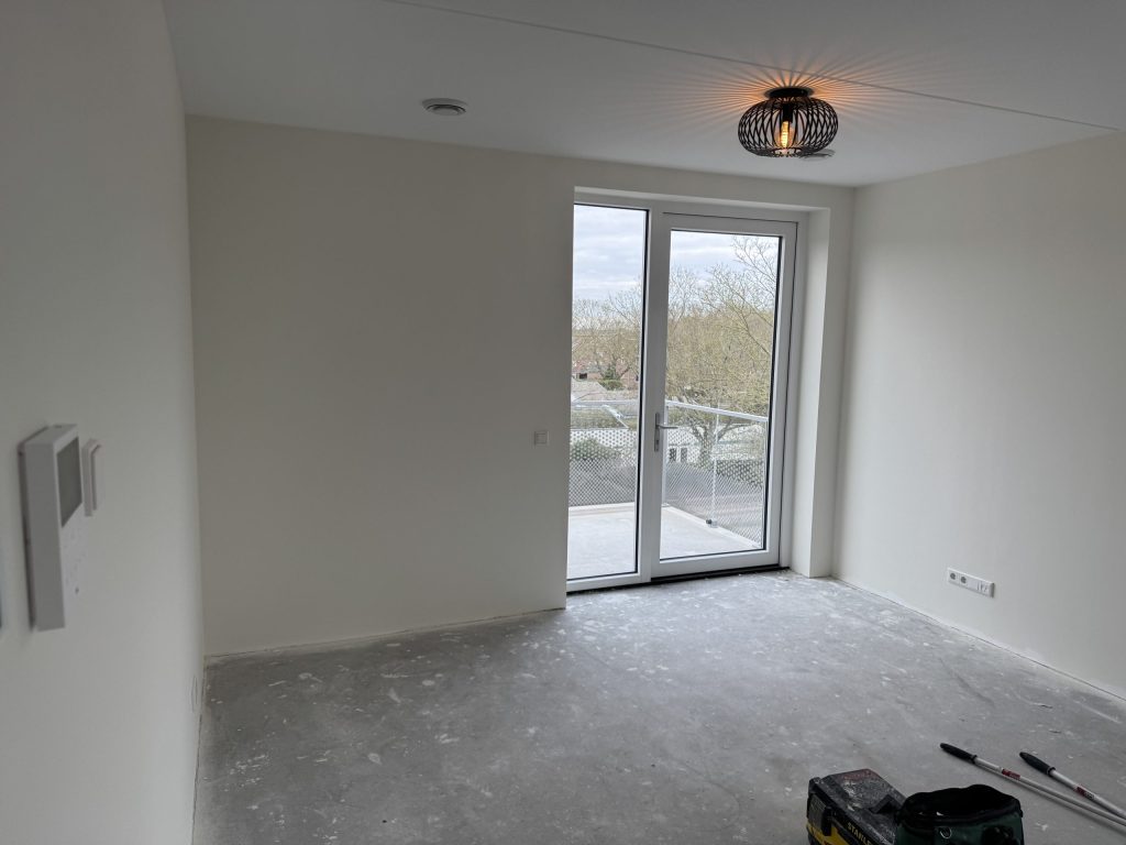 Kale kamer van een net opgeleverd appartement met balkondeuren, lichte wanden en een betonvloer