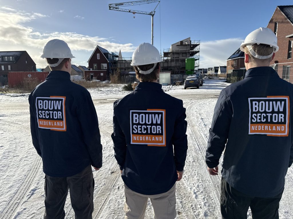 Drie vakmensen van Bouwsector Nederland met witte helm kijken naar nieuwbouwhuizen in aanbouw